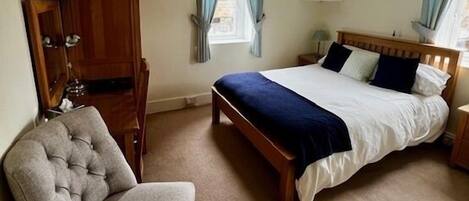 A bedroom with a bed, a chair, a wardrobe, and a window with curtains.