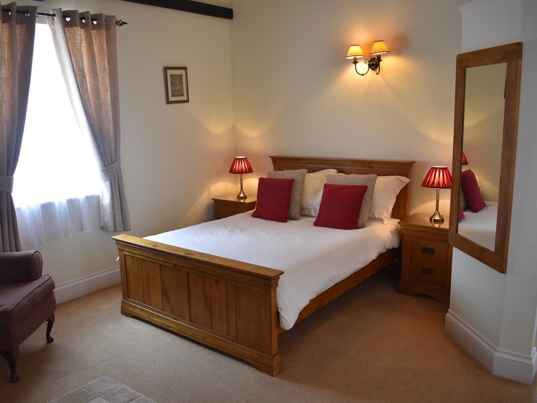 A neatly made bed with red pillows, a wooden headboard, and bedside lamps.