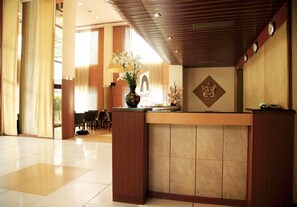 A hotel reception area with a reception desk, chairs, a vase with flowers, and a clock on the wall. - Harrisons Hotel (Chennai)