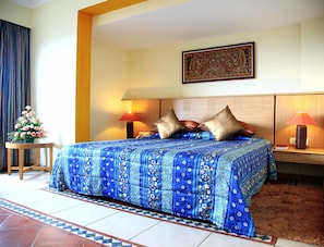 A hotel room with a large bed, two bedside lamps, a floral arrangement, and a patterned rug. - Harrisons Hotel (Chennai)