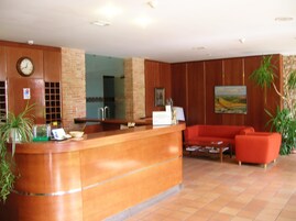 Zona de recepción con un mostrador de madera, un reloj, un sofá rojo y plantas en macetas.