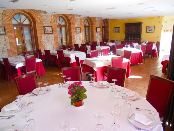 Un restaurant avec de nombreuses tables dressées pour le service, avec des chaises rouges et des nappes blanches.