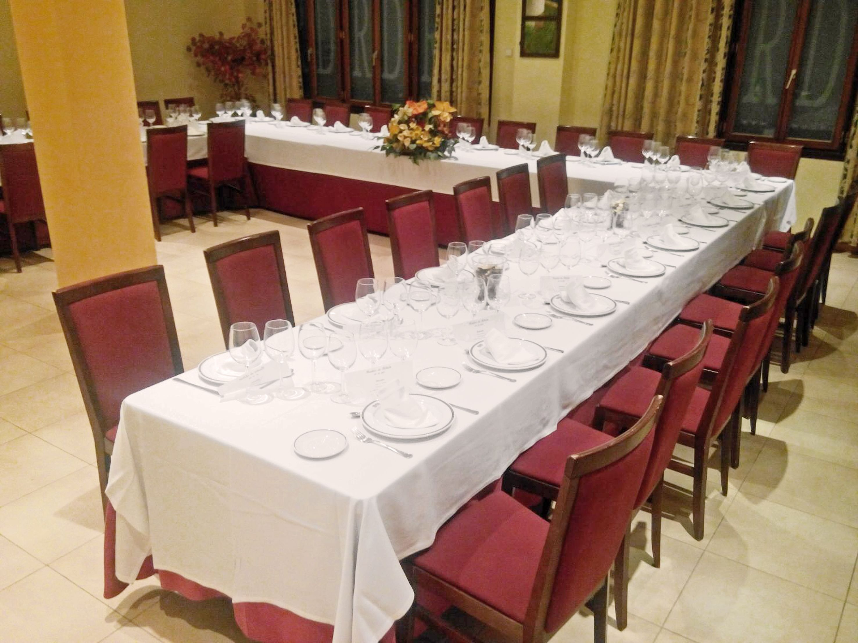 A long dining table set with white tablecloths, red upholstered chairs, and clear glassware.