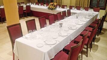 A long dining table set with white tablecloths, red upholstered chairs, and clear glassware.