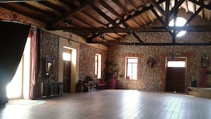 A spacious room with a tiled floor, stone walls, wooden beams, and a large window allowing natural light. - AM Ribera del Duero (Penafiel)