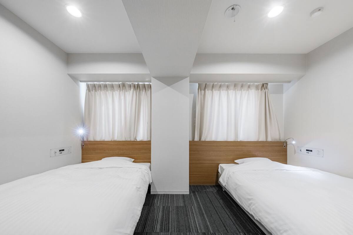 A hotel room with two single beds, a wooden headboard, a carpeted floor, and a ceiling light.