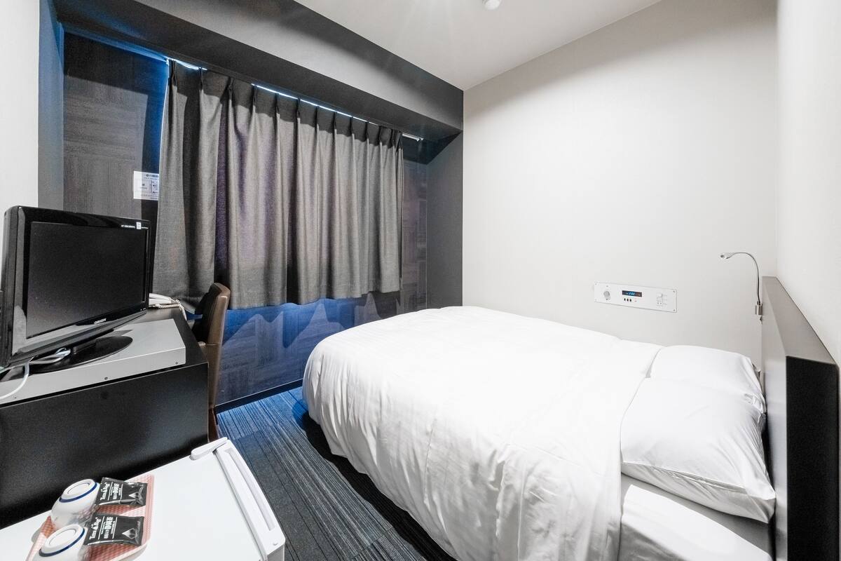 A hotel room with a bed, a desk with a computer, a chair, and a TV.