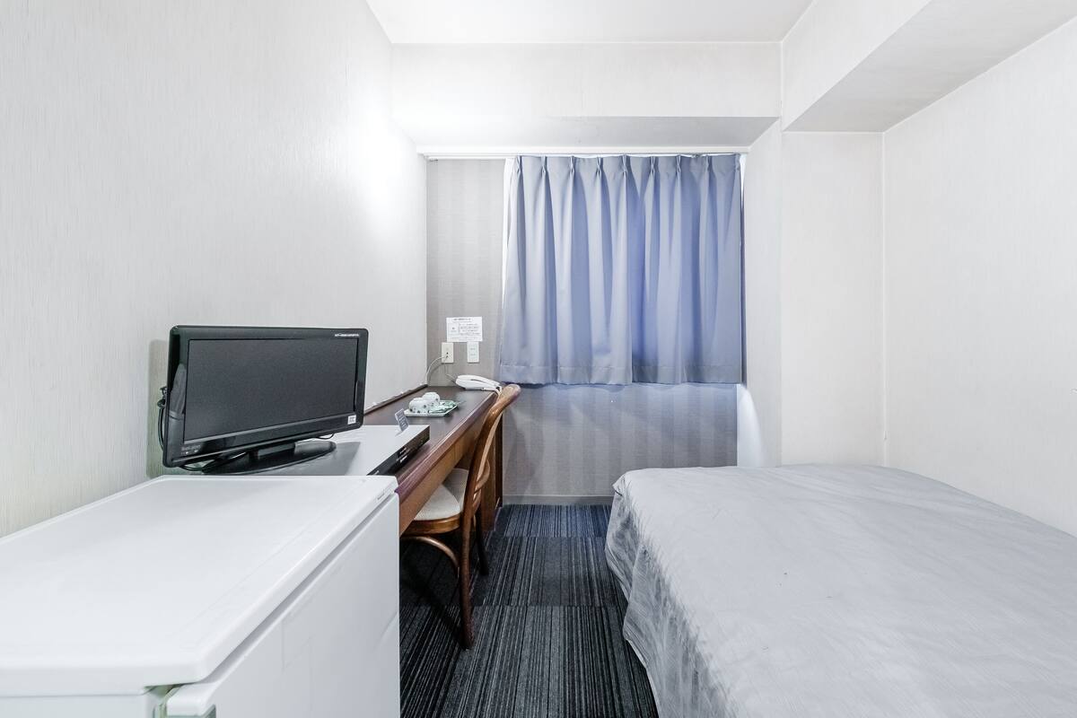 A hotel room with a bed, a desk with a computer, a telephone, and a small refrigerator.