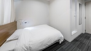 A hotel room with a single bed, a wooden headboard, a white wall, a door, and a small window. - Tabist Annex Hotel Tetora Hakodate Goryokaku (Hakodate)