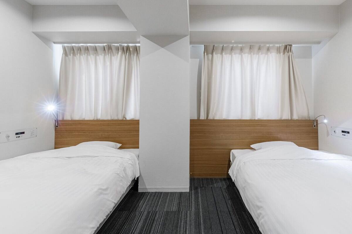 A hotel room with two single beds, a wooden headboard, a light switch, and a power outlet on the wall.