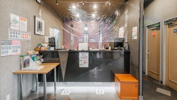 A reception area with a counter, a wooden bench, and a sign indicating the front. - Tabist Annex Hotel Tetora Hakodate Goryokaku (Hakodate)