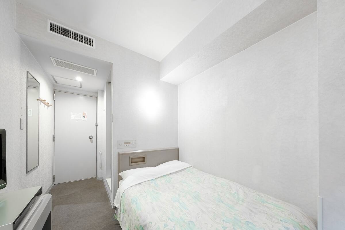 A hotel room with a bed, a bedside table, a mirror, and a wall-mounted TV.
