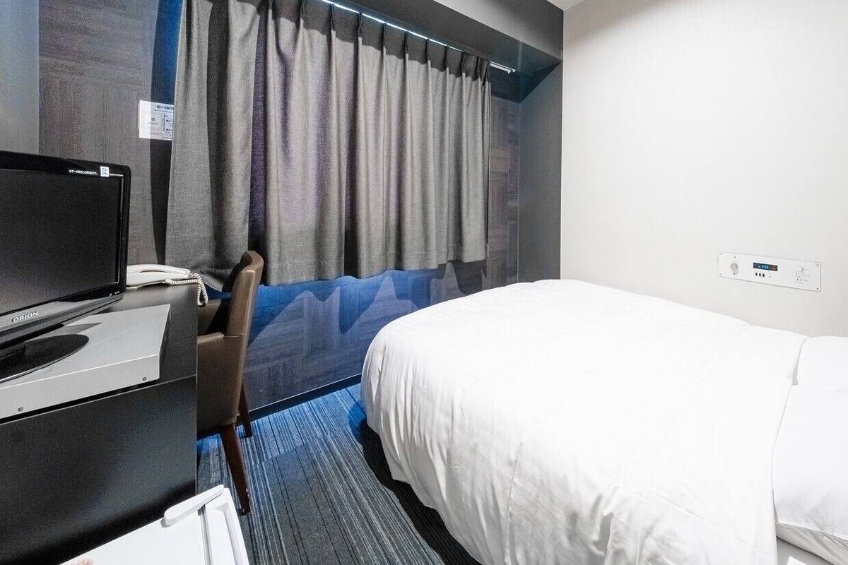 A hotel room with a bed, a desk with a computer, a telephone, and a window with curtains.