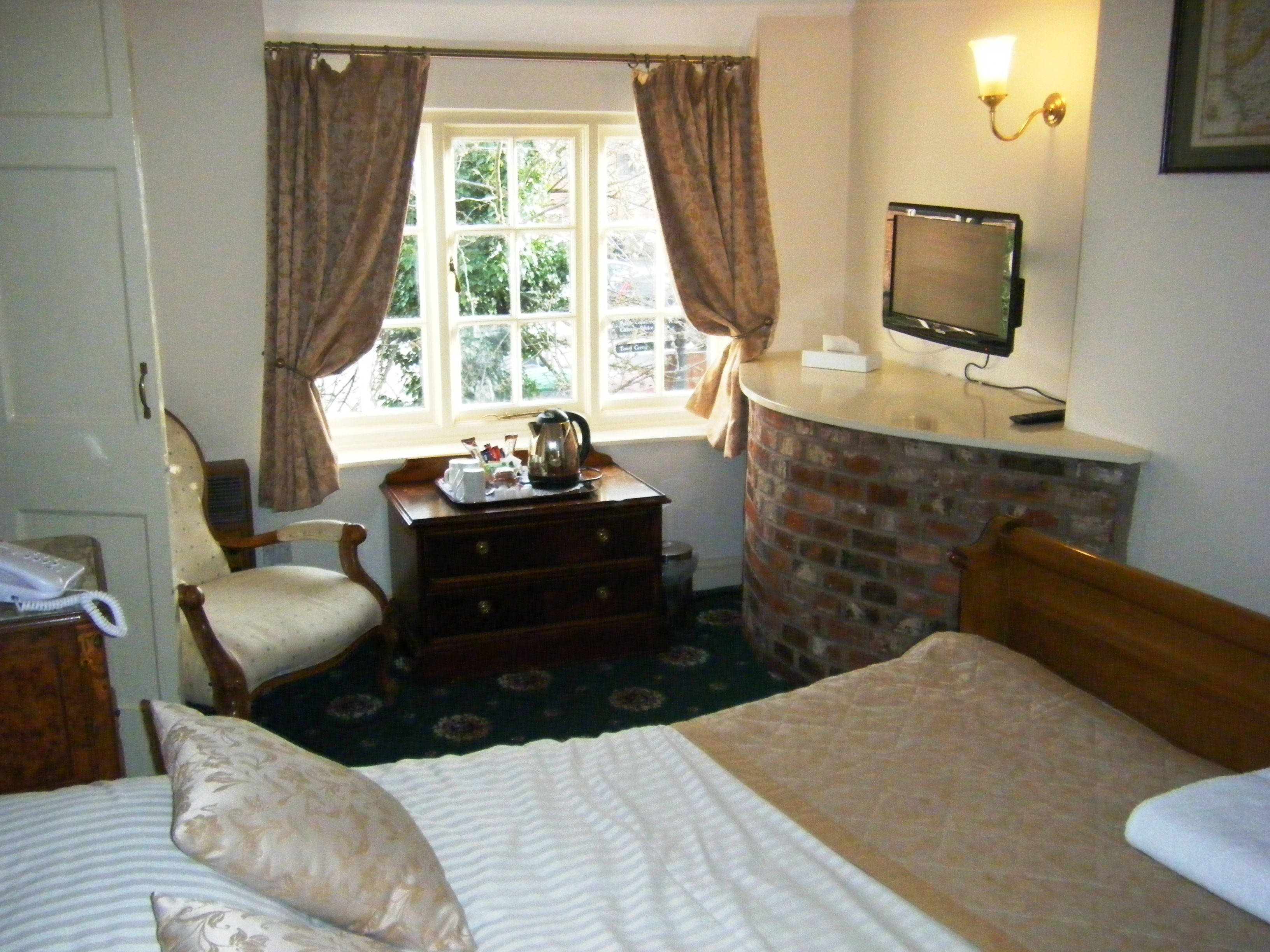 A hotel room with a bed, a dresser, a chair, a desk with a kettle, a television, and a window with curtains.