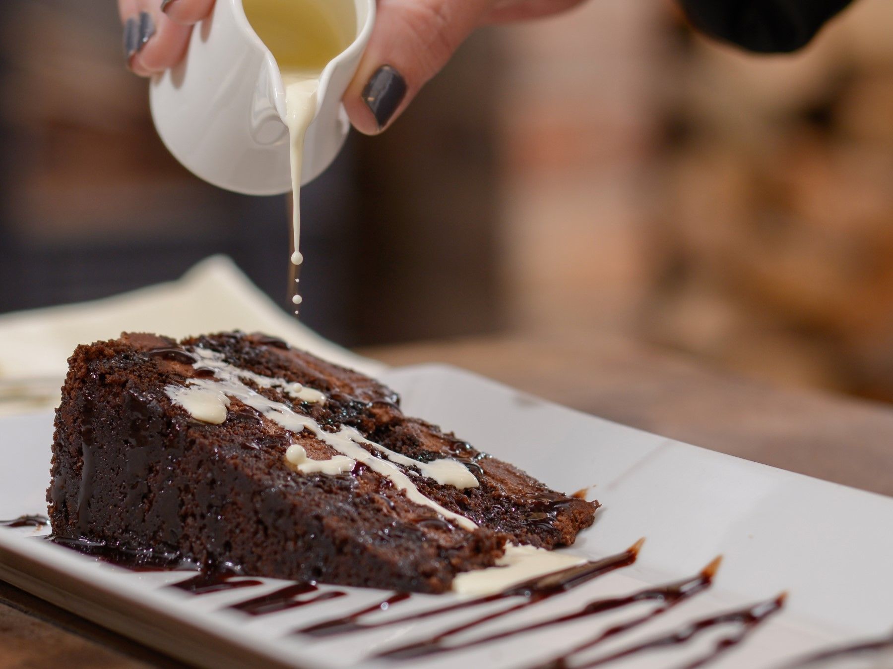 A slice of chocolate cake with white icing and chocolate sauce on a plate.