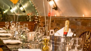 Una larga mesa de comedor dispuesta con varias copas de vino, una botella de champán y un adorno dorado.