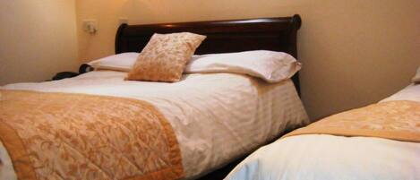 Habitación de hotel con dos camas, cada una con cabecero de madera, ropa de cama blanca y una manta decorativa.