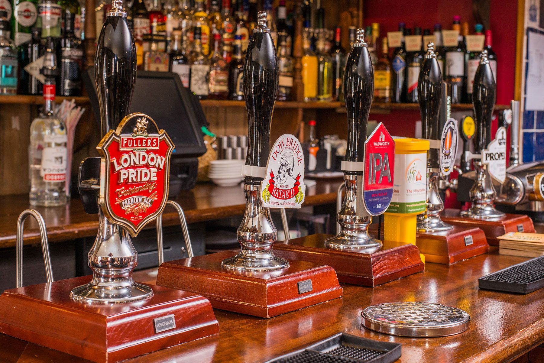 Un bar con múltiples grifos de cerveza, incluyendo Fuller's London Pride y Dow Bridge IPA.