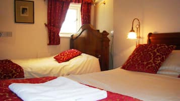 A hotel room with two beds, red and white bedding, a window with red curtains, and a wall-mounted lamp.