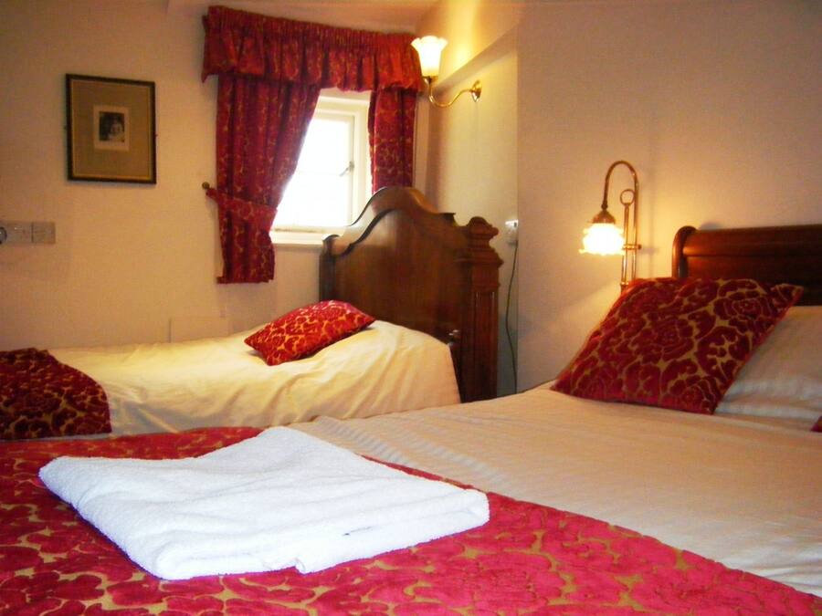 A hotel room with two beds, red and white bedding, a window with red curtains, and a wall-mounted lamp.