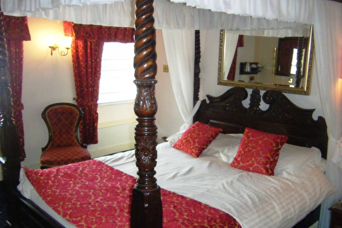 A four-poster bed with a wooden headboard, red and white bedding, and a mirror above it.