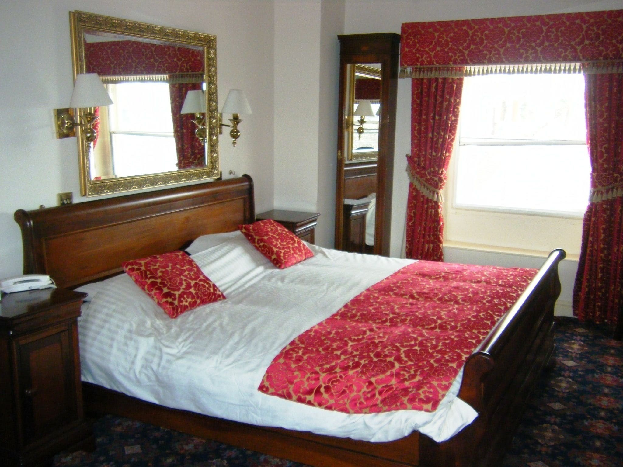 Uma cama bem arrumada com lençóis brancos e vermelhos, uma cabeceira de madeira e um edredom vermelho estampado.