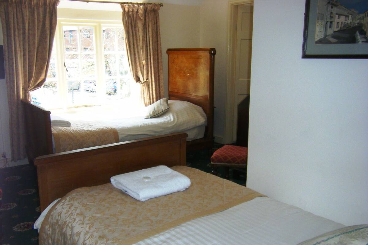 A hotel room with two beds, a wooden headboard, a window with curtains, and a framed picture on the wall.