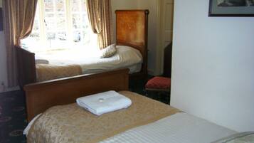 A hotel room with two beds, a wooden headboard, a window with curtains, and a framed picture on the wall.