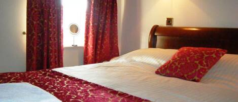 Una cama bien hecha con una colcha de diseño rojo y blanco, una única almohada roja, y una lámpara montada en la pared.