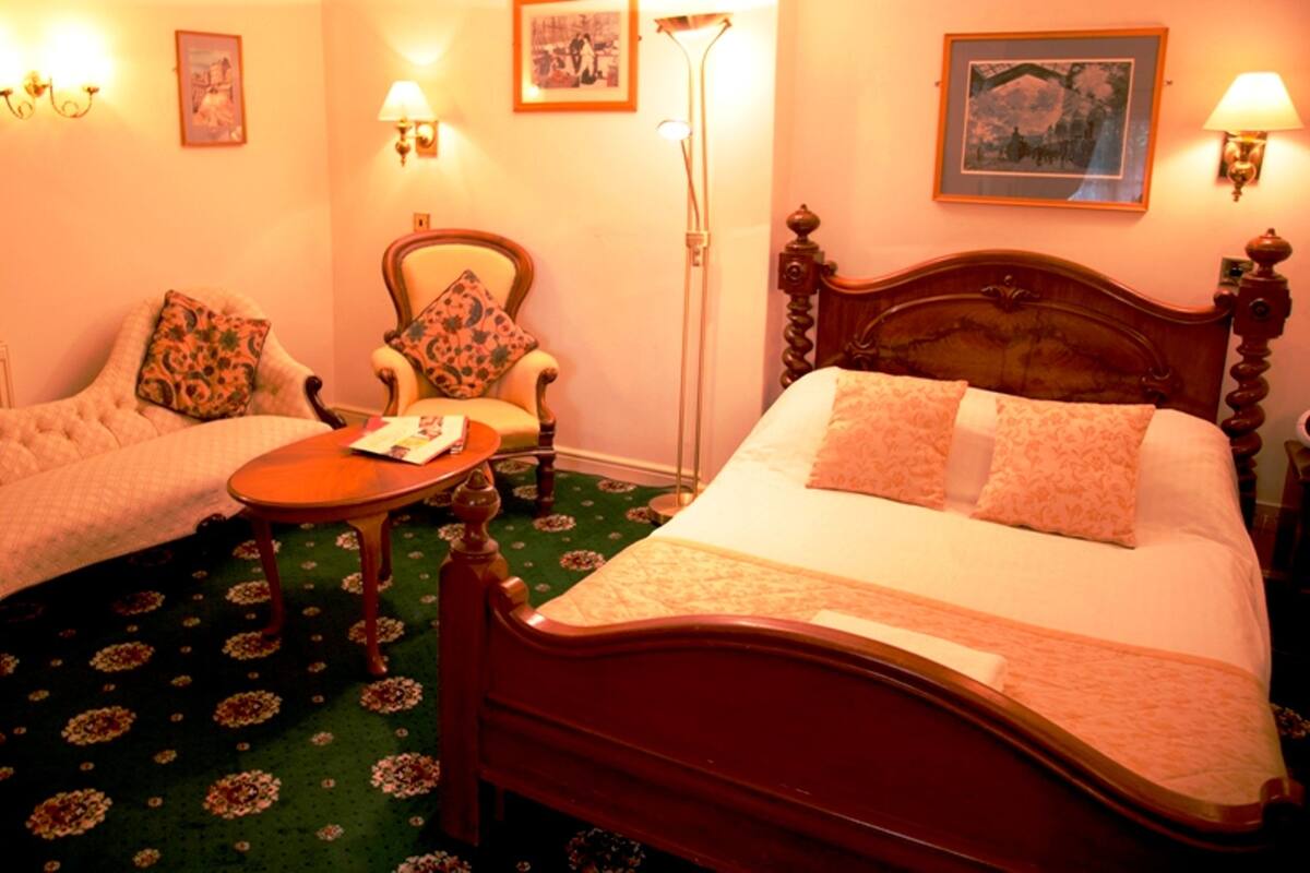 A hotel room with a large bed, two armchairs, a small table, and a floor lamp.