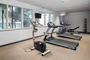 Un gimnasio con dos cintas de correr, una elíptica y una pantalla de televisión en la pared.