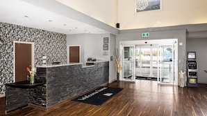 A reception area with a stone counter, a welcome mat, an ATM, and a glass door entrance.