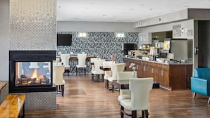 A modern hotel lobby with a fireplace, seating area, and a breakfast bar.