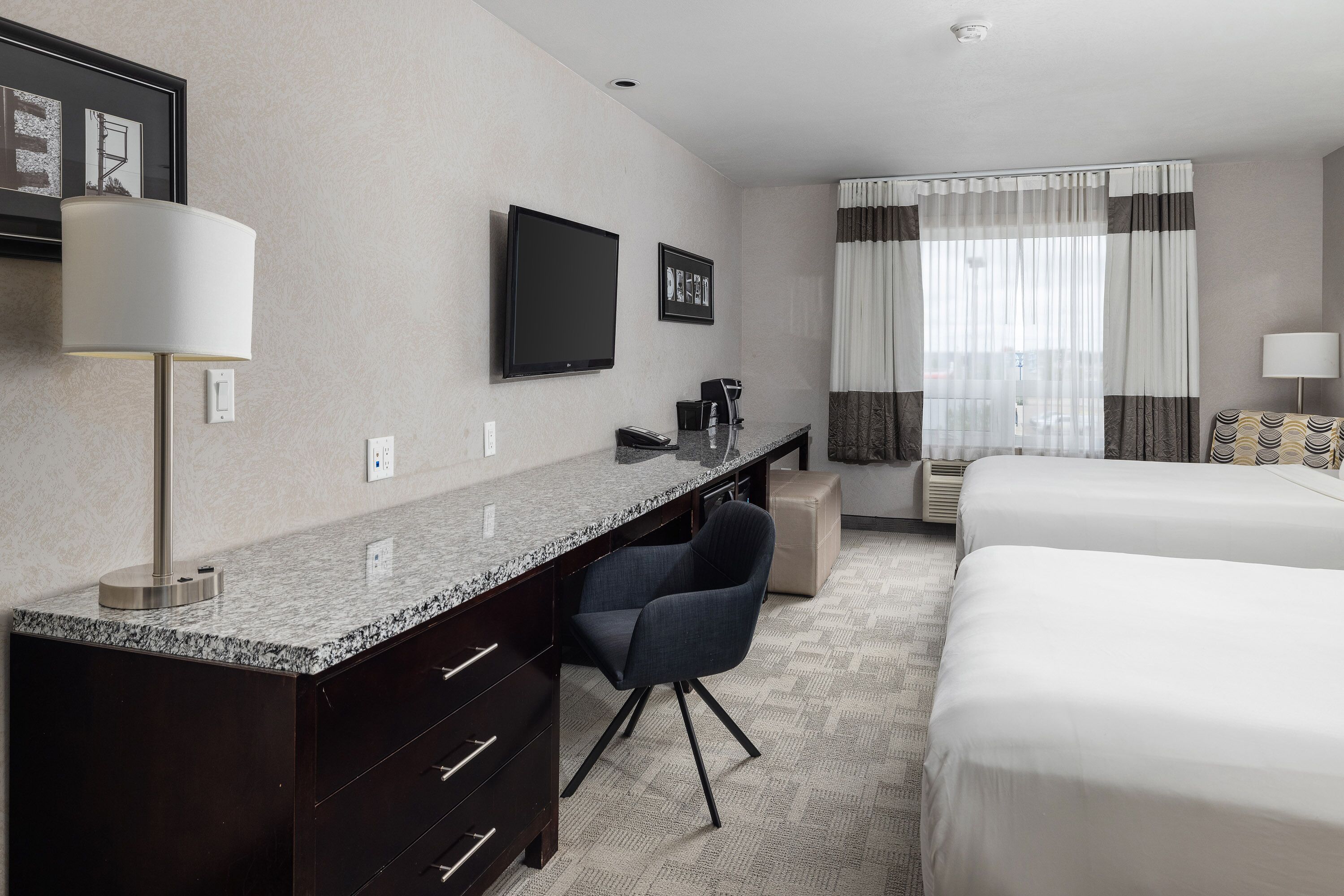 A hotel room with a bed, a desk with a chair, a TV, and a window with curtains.