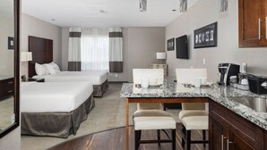 A hotel room with two beds, a kitchen area with a marble countertop, and a dining table with chairs.