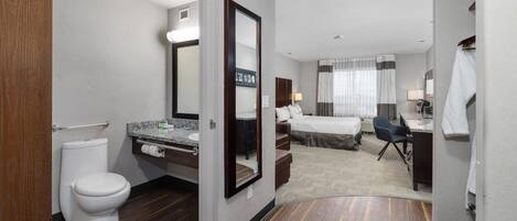 Quarto de hotel com banheiro, cama, escrivaninha e cadeira.