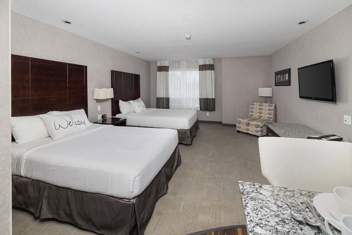 A hotel room with two beds, a sofa, a TV, and a small table with a tray.