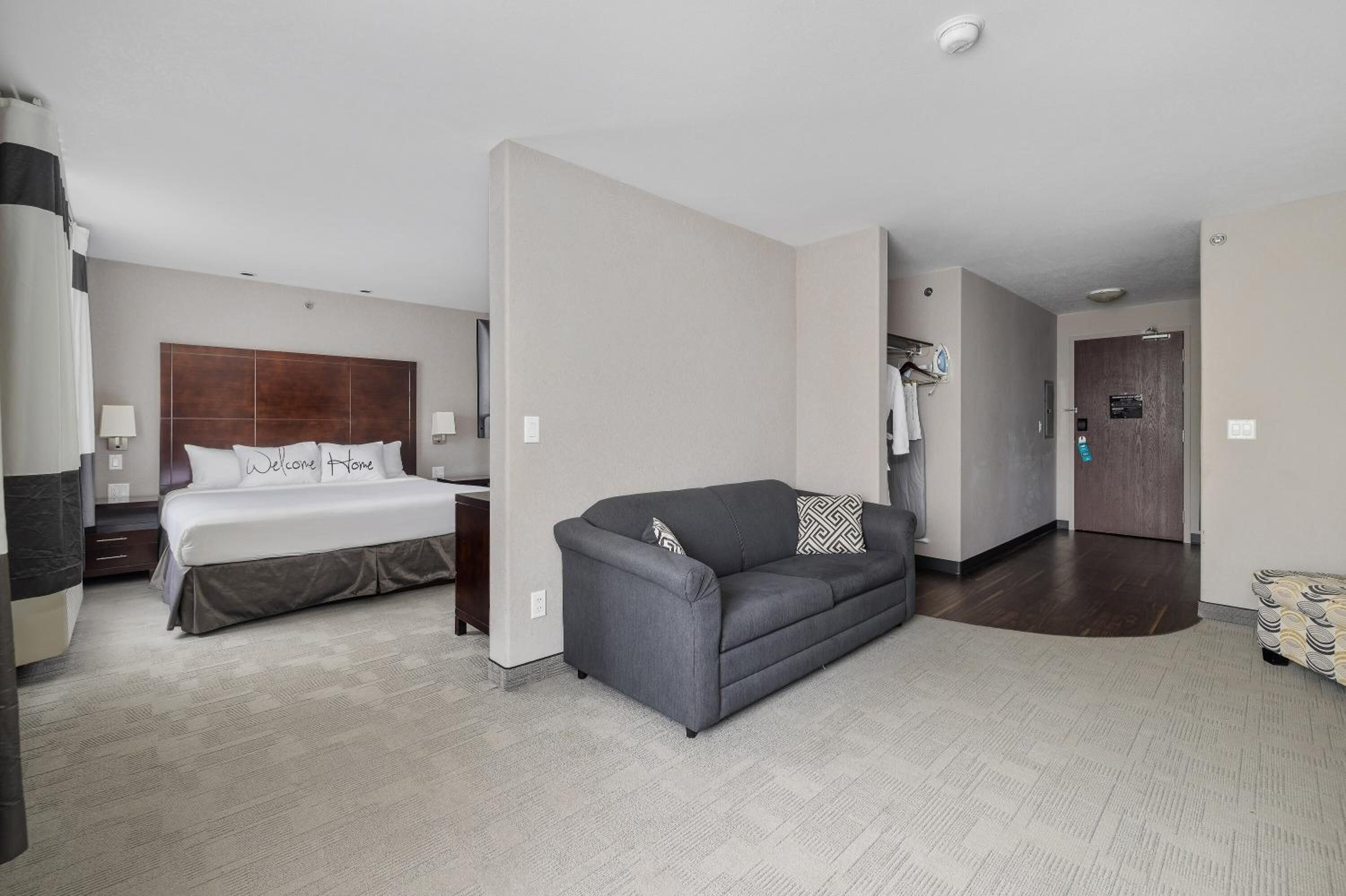 Una habitación de hotel con una cama, un sofá gris y un cabecero de madera.