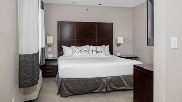 A hotel room with a large bed, two bedside tables, a flat-screen TV, and a dark wooden headboard.