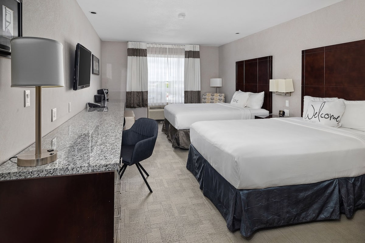 A hotel room with two beds, a desk, a chair, a TV, and a window with curtains.