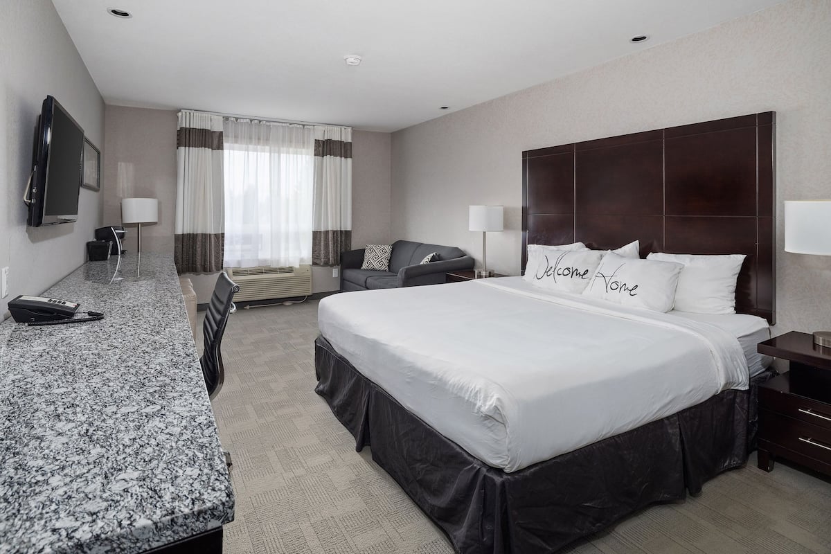 A hotel room with a large bed, a desk with a telephone, a flat-screen TV, and a window with curtains.