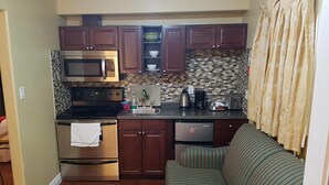 A compact kitchen with a microwave, oven, and coffee maker. There is a striped sofa in the living area. - Bayside Inn & Waterfront Suites (Kingston)