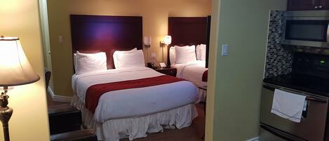 A hotel room with a large bed, a desk, a lamp, a microwave, and an oven.