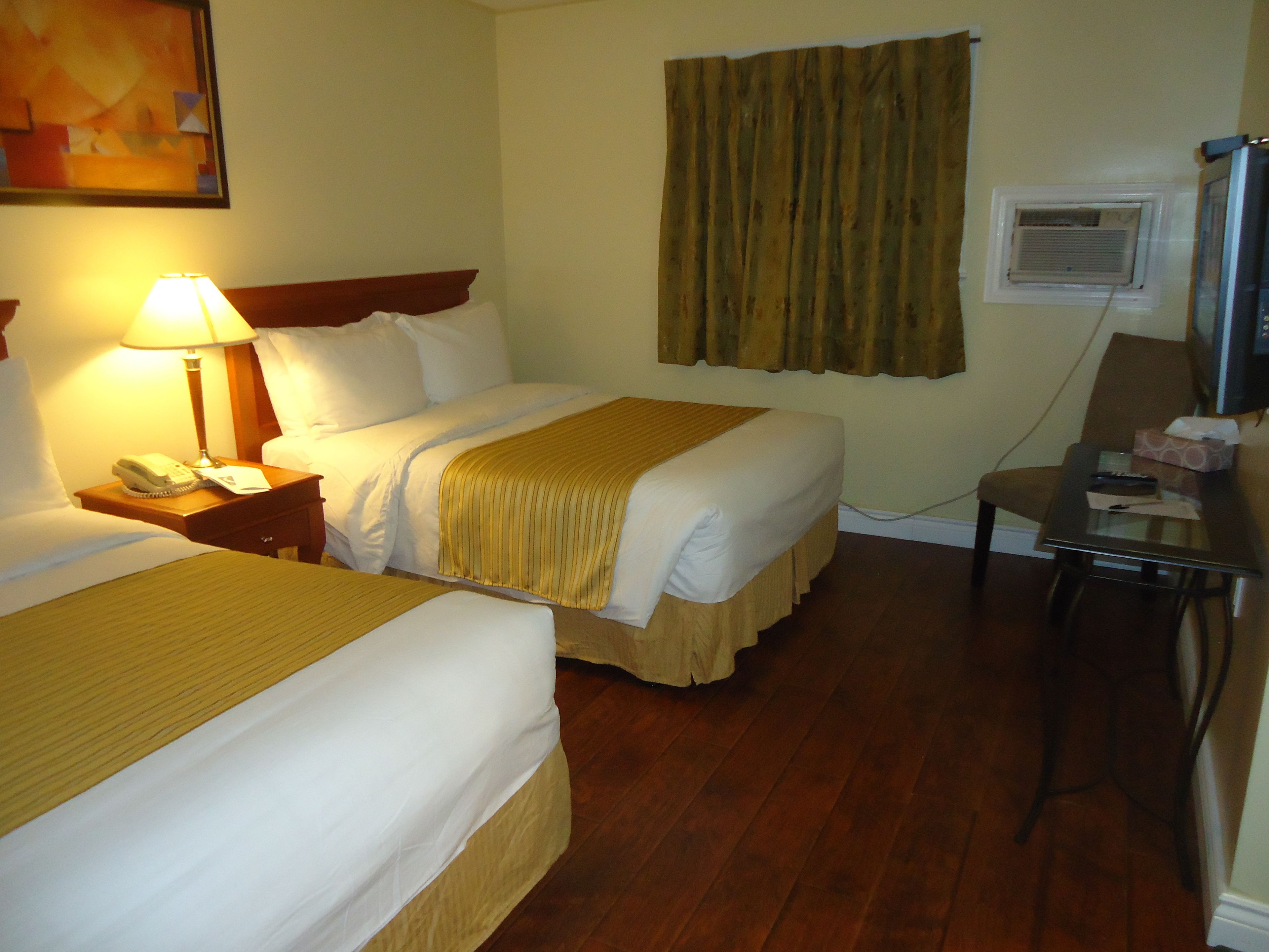 A hotel room with two beds, a desk, a chair, a lamp, a telephone, and a painting on the wall.