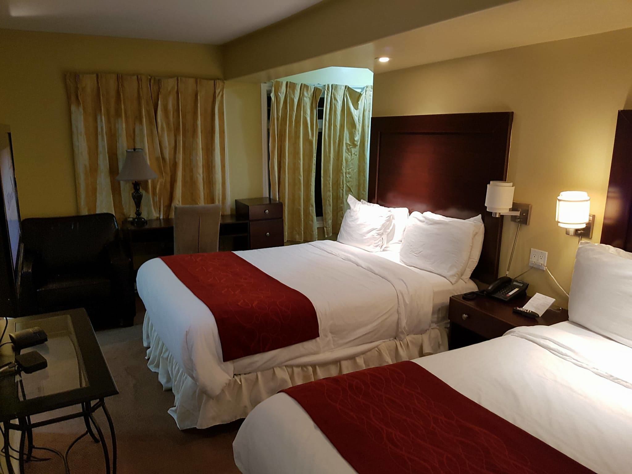 Quarto de hotel com duas camas, uma escrivaninha, uma cadeira, um abajur e uma mesa de cabeceira com telefone.
