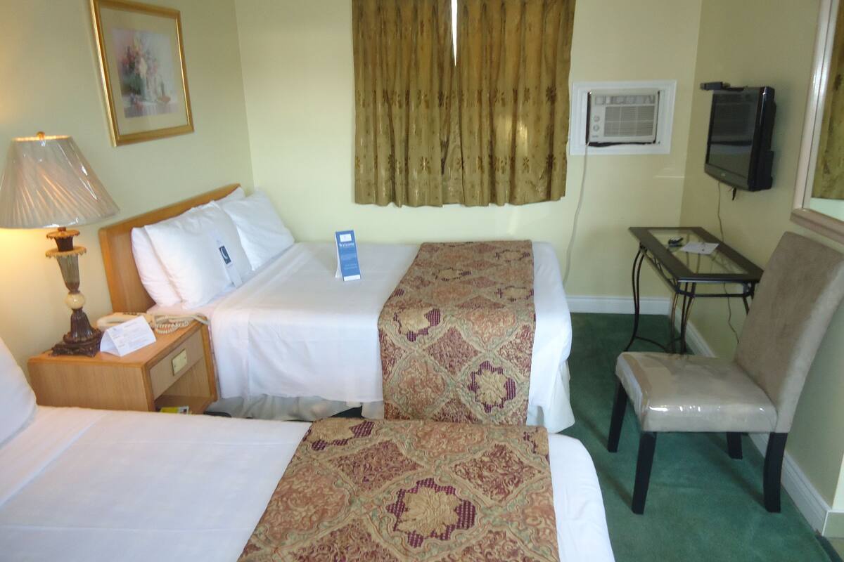 Une chambre d’hôtel avec deux lits, un bureau, une chaise, une télévision et une fenêtre avec des rideaux.