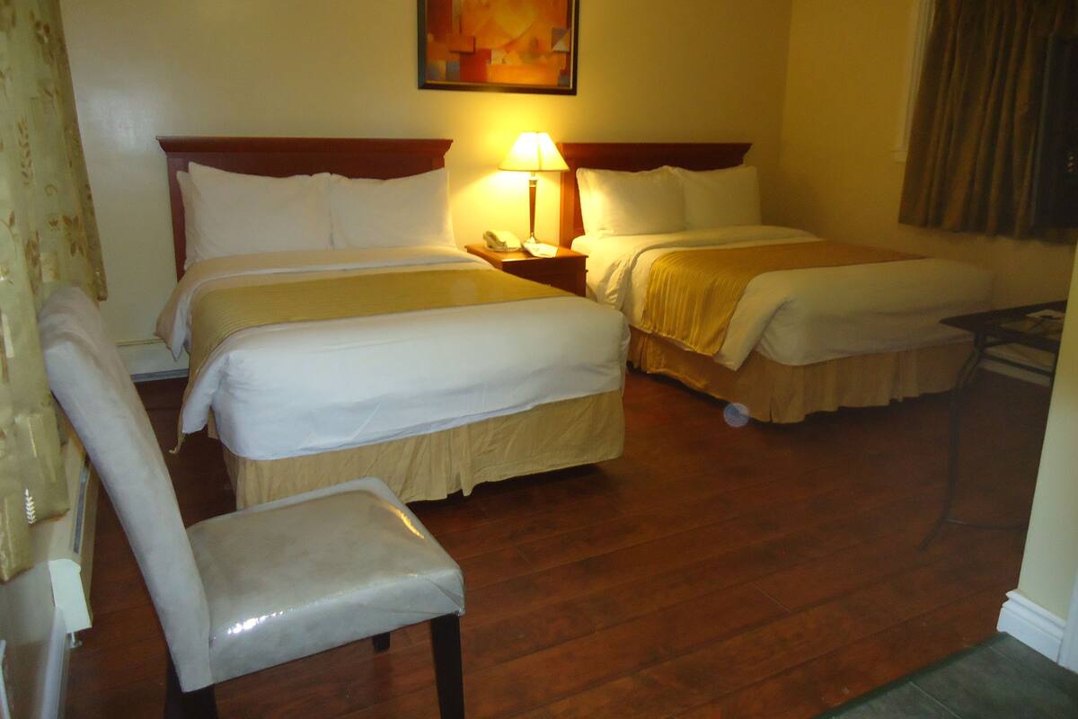 Une chambre d’hôtel avec deux lits, une chaise, une table de chevet avec une lampe et un tableau au mur.