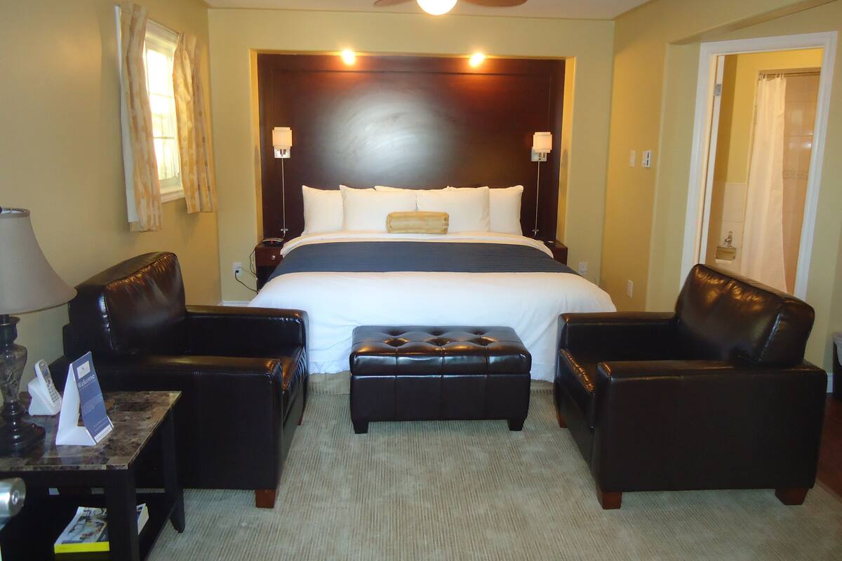 Une chambre d’hôtel avec un grand lit, deux fauteuils, une petite table et un ventilateur de plafond.