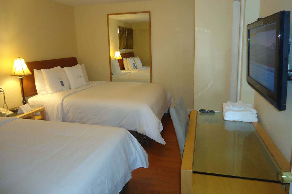 Une chambre d’hôtel avec deux lits, une table de chevet avec une lampe, un téléviseur posé sur un meuble et un miroir au mur.