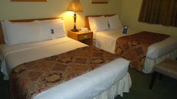 A hotel room with two beds, a nightstand, a lamp, and a chair.